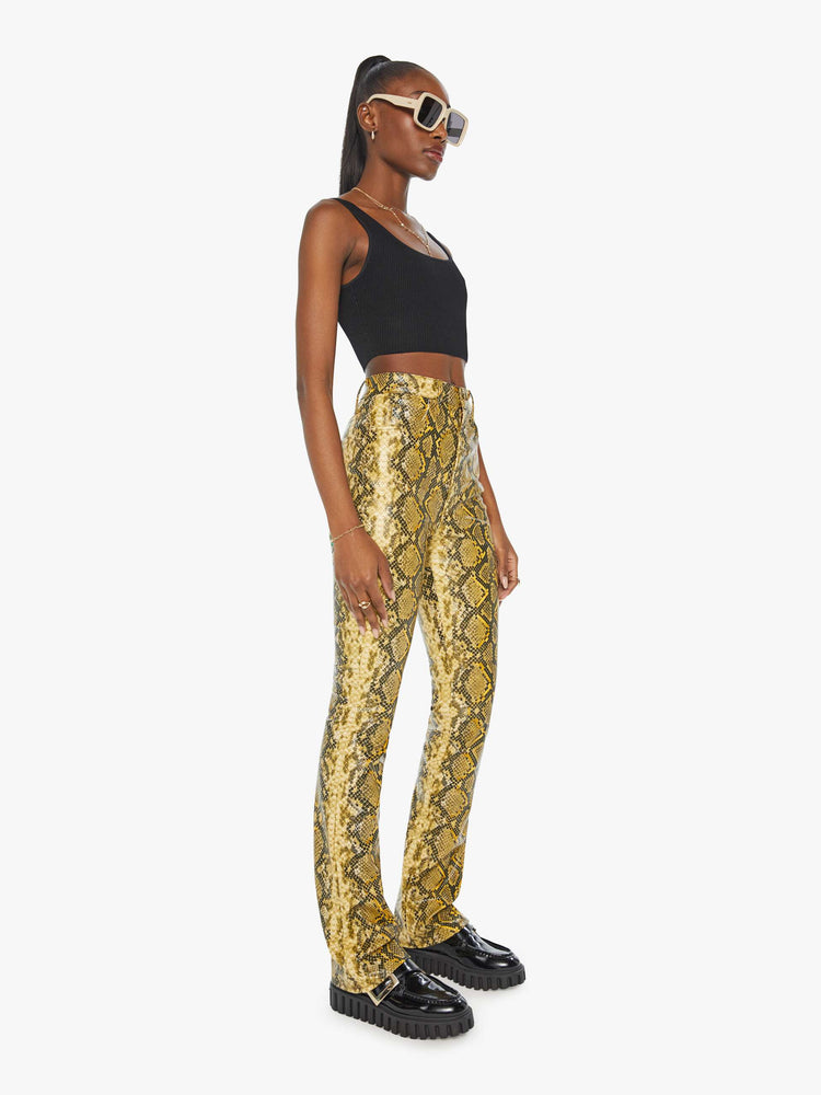 Side angle view of a woman in a yellow and black faux snakeskin super high-waisted pants with a flared leg and a long 34-inch inseam with a clean hem.