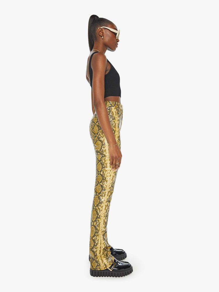 Side view of a woman in a yellow and black faux snakeskin super high-waisted pants with a flared leg and a long 34-inch inseam with a clean hem.