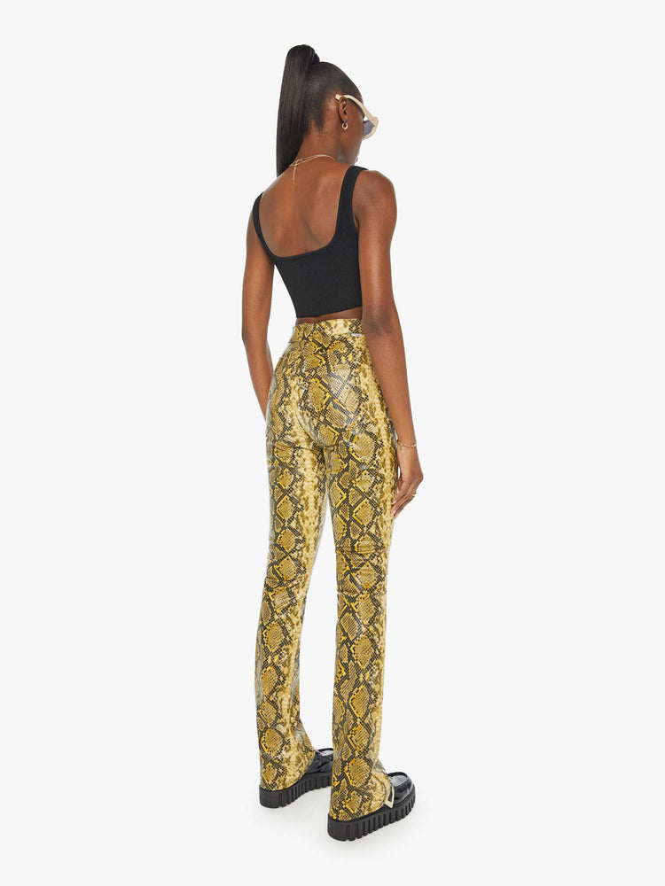 Back view of a woman in a yellow and black faux snakeskin super high-waisted pants with a flared leg and a long 34-inch inseam with a clean hem.