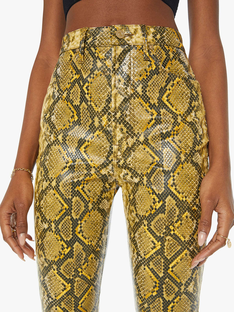 Close up view of a woman in a yellow and black faux snakeskin super high-waisted pants with a flared leg and a long 34-inch inseam with a clean hem.