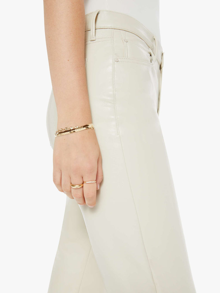 Close up view of a woman in a high-waisted pants with a wide straight leg, zip fly and an ankle-length inseam with a clean hem in cream leather pants.