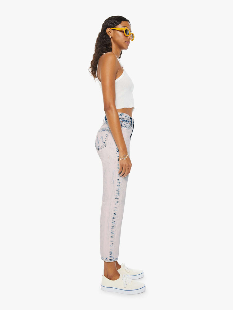 side view of a woman in ankle length jeans that are acid-washed and overdyed in a soft light pink with darker spots throughout.