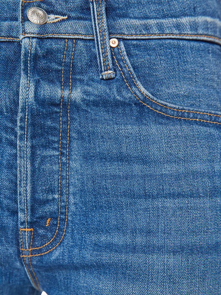 Close up  view of a woman in a high-rise flare with a button fly and frayed ankle-length hem in a med blue wash.