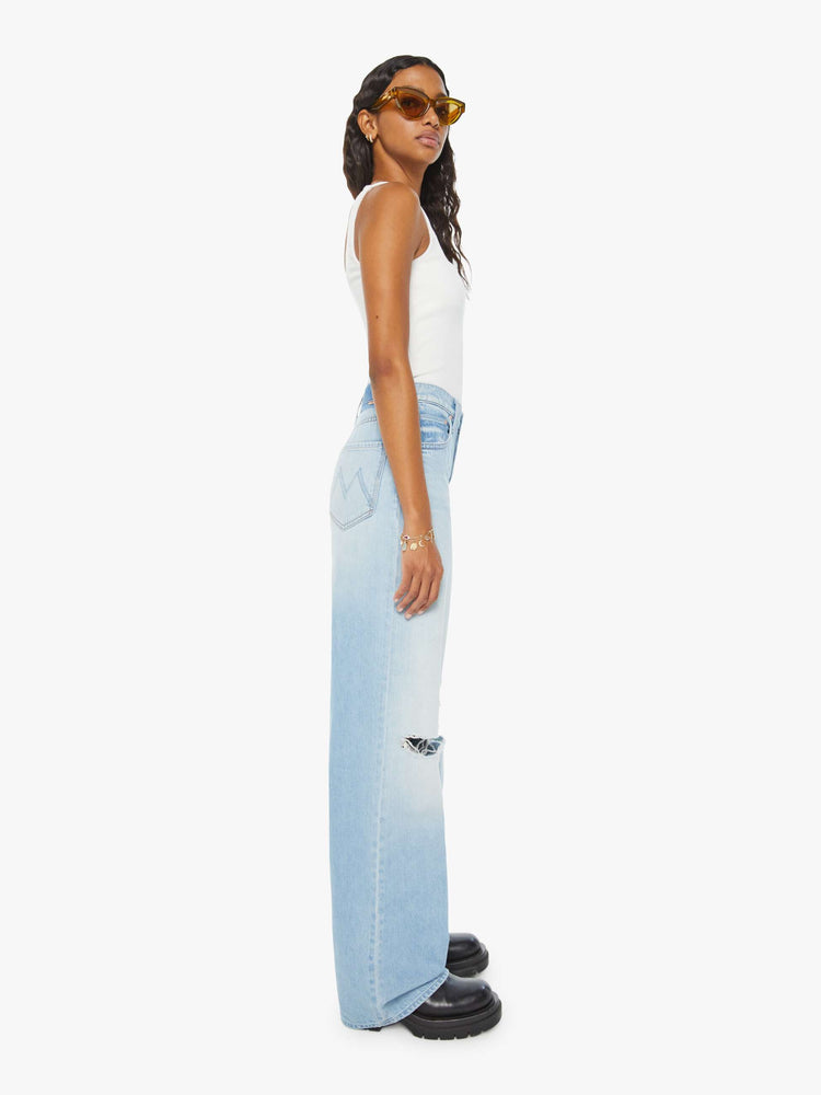 Side view of a woman in light blue super high-rise jeans with a loose wide leg, zip fly and a long 34-inch inseam with a clean hem. 