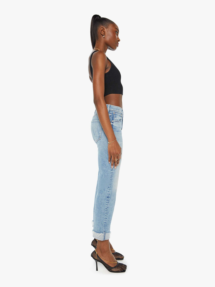 Side view of a woman in a light blue button fly jean with a high rise and ankle length hem thats cuffed and frayed.