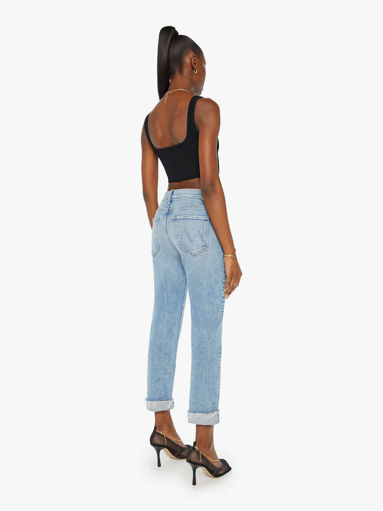 Back view of a woman in a light blue button fly jean with a high rise and ankle length hem thats cuffed and frayed.