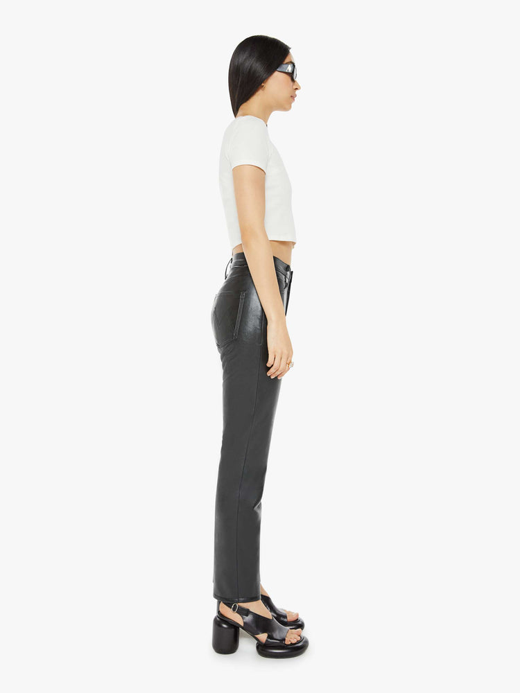 Side view of a woman in a recycled black leather high waisted straight-leg pants with a 31-inch inseam and a clean hem.