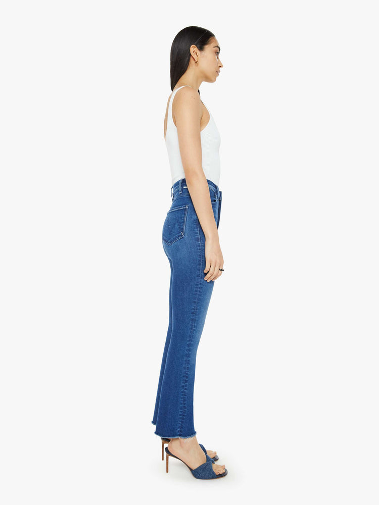 Side view of a woman dark blue high-rise bootcut has a 28.25-inch inseam and a frayed hem.