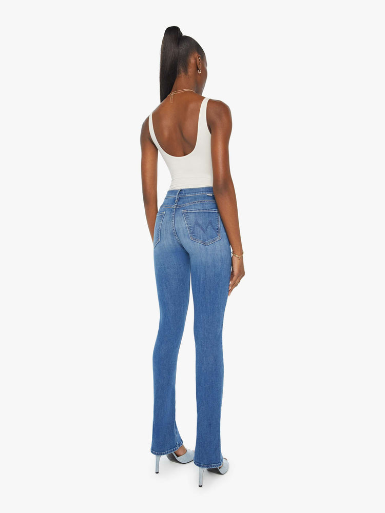 Back view of a woman in a med blue high-rise straight leg jean with a long 34-inch inseam and a split front hem.