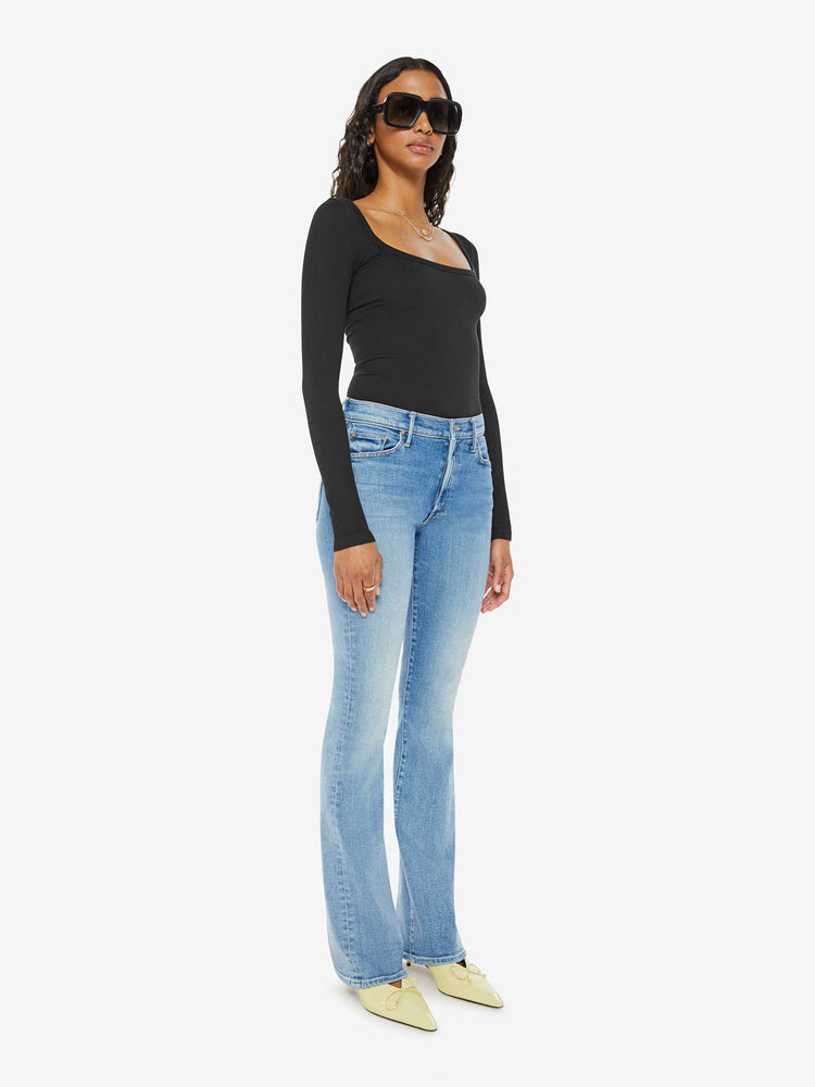 Side angle view of a woman midblue wash flare jeans with a mid rise and a long 32-inch inseam with a clean hem.