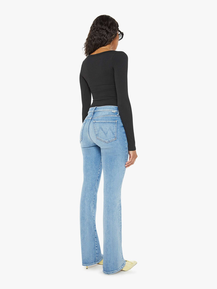 Back view of a woman midblue wash flare jeans with a mid rise and a long 32-inch inseam with a clean hem.