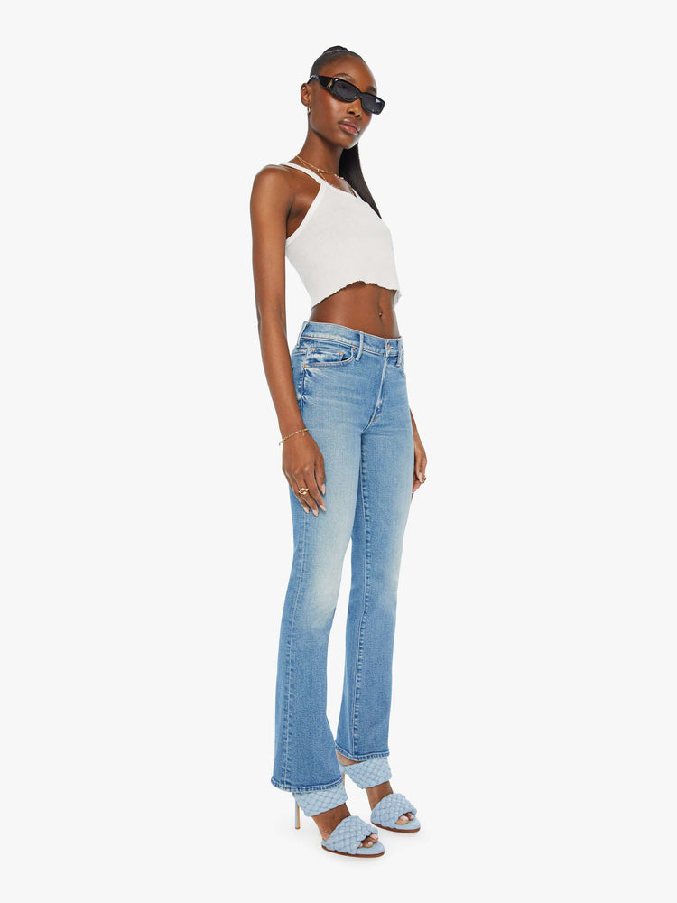 Side angle view of a woman in mid rise flare jean in a light blue wash. 