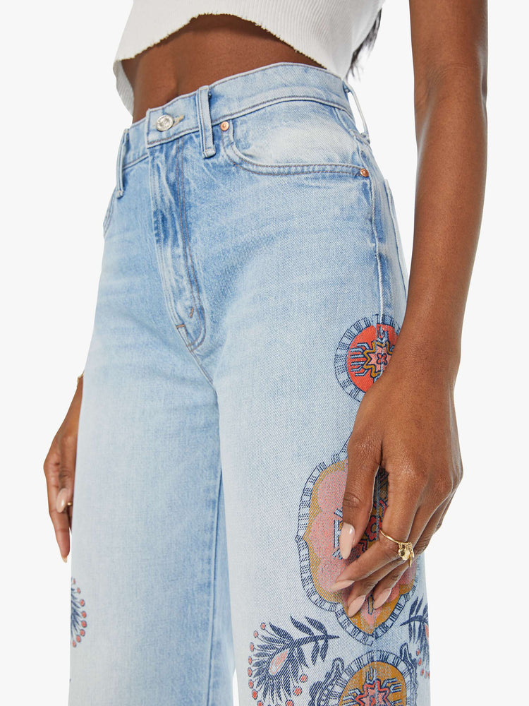 Close up view of a high rise wide leg jean in a light blue wash with printed pattern down the side of each leg.