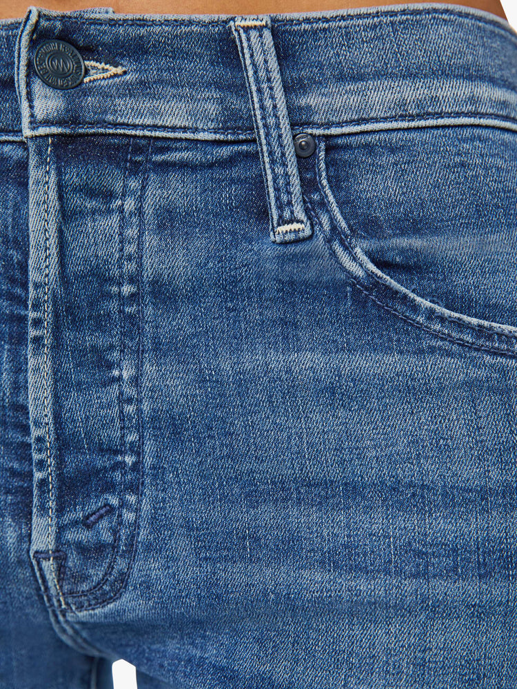 Detailed view of a woman in medium blue slim straight-leg (adopted from our men’s line) featuring a mid rise, button fly, low-set back pockets and a clean hem.