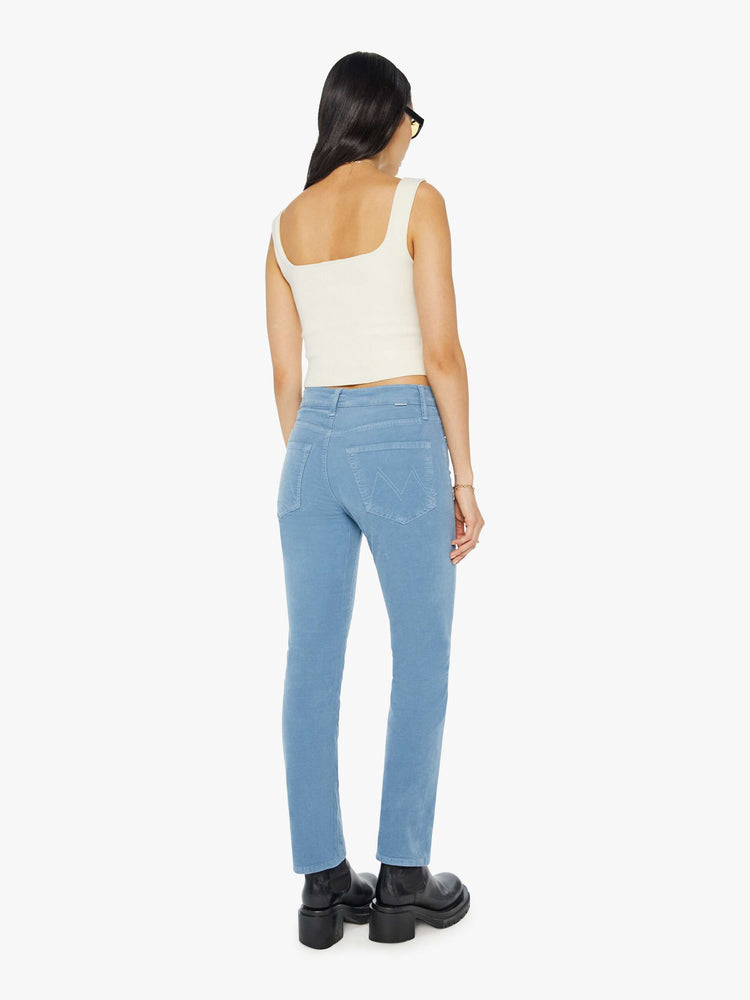 Back view of a woman in light blue corduroy slim straight-leg pants that feature a mid rise, button fly, low-set back pockets and a clean hem.