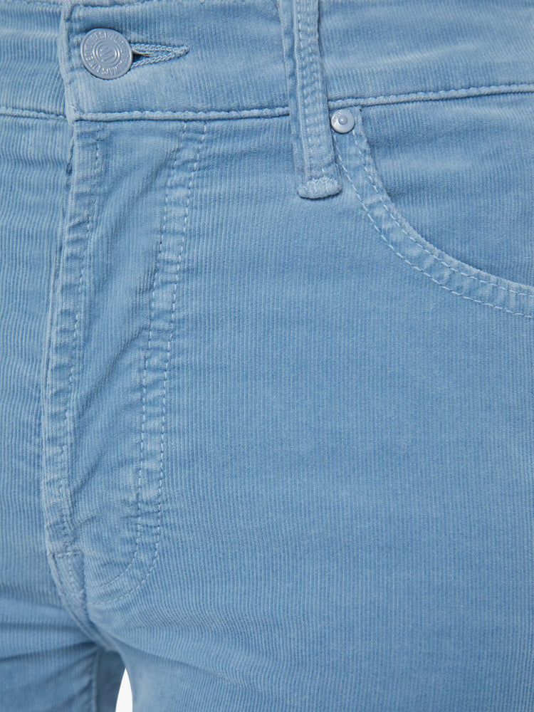 Detailed view of a woman in light blue corduroy slim straight-leg pants that feature a mid rise, button fly, low-set back pockets and a clean hem.