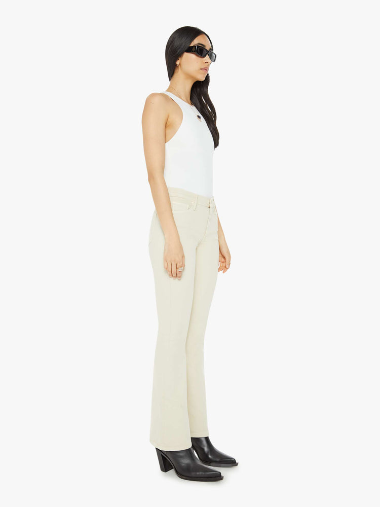 Side angle view of a woman in an off white color flare jean has a mid rise with a 32-inch inseam and a clean hem.