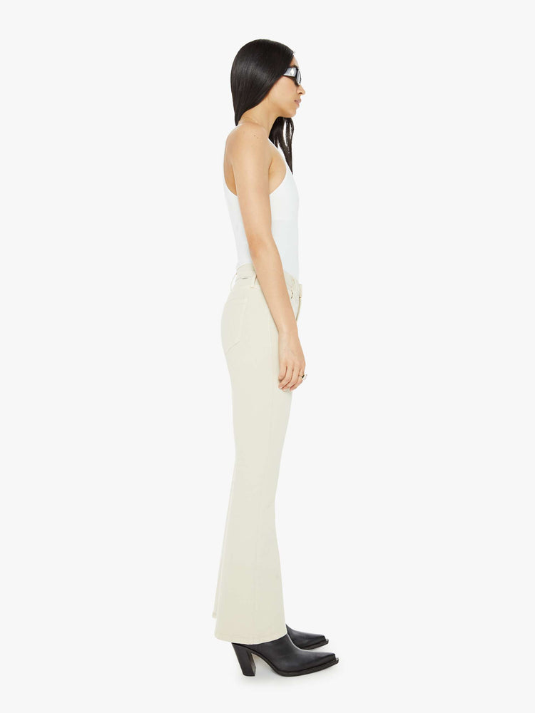 Side view of a woman in an off white color flare jean has a mid rise with a 32-inch inseam and a clean hem.