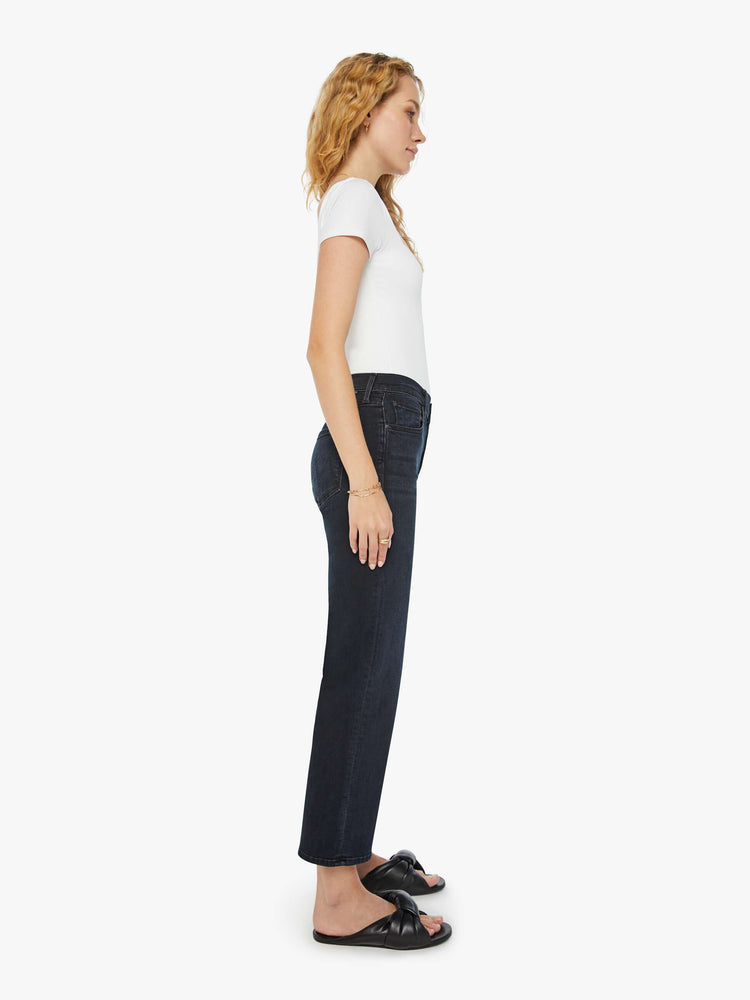 Side view of a woman in a dark denim mid-rise jean with a wide straight leg, zip fly and clean ankle-length inseam.