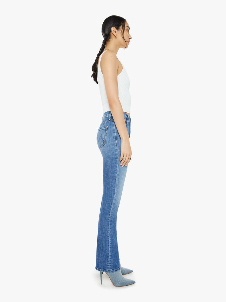 Side view of a woman in a high-waisted bootcut has a 32-inch inseam and a clean hem in a mid blue wash.