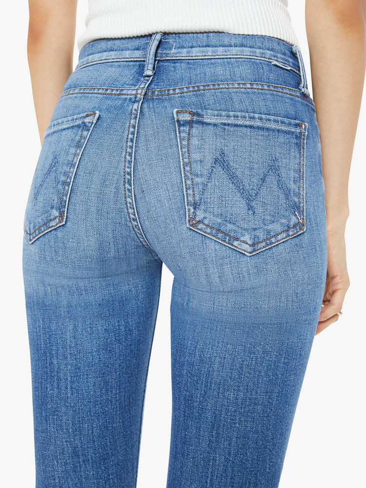 Waist close up view of a woman in a high-waisted bootcut has a 32-inch inseam and a clean hem in a mid blue wash.