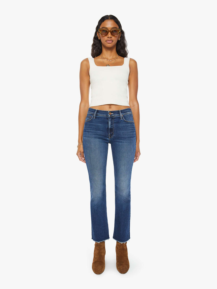 Front view of a woman narrow flare jeans with a mid rise and an ankle-length inseam with a frayed hem in a dark blue wash.