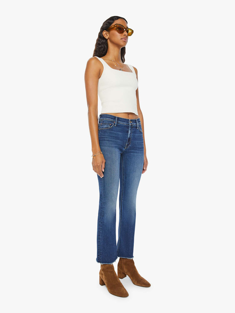 Angled view of a woman narrow flare jeans with a mid rise and an ankle-length inseam with a frayed hem in a dark blue wash.