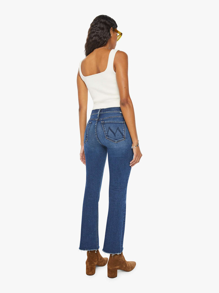 Back view of a woman narrow flare jeans with a mid rise and an ankle-length inseam with a frayed hem in a dark blue wash.