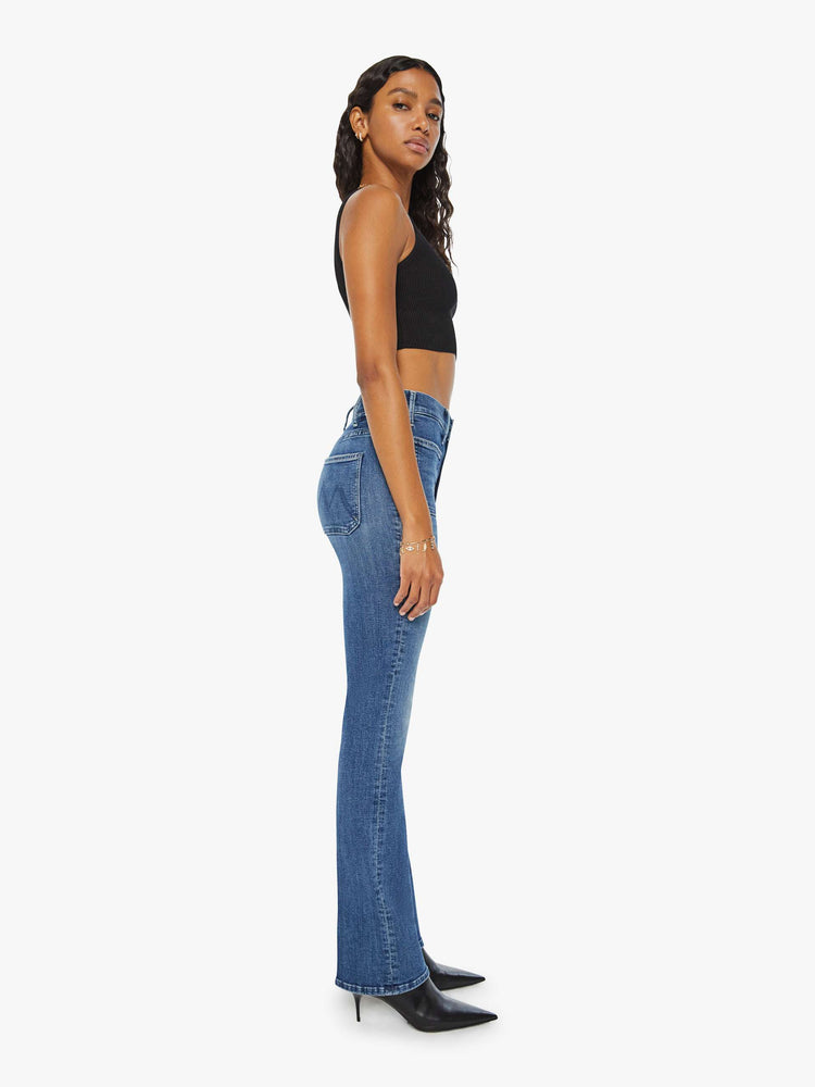 Side view of a woman high-rise bootcut is designed with front patch pockets, a long 32-inch inseam and a clean hem in a mid blue wash.