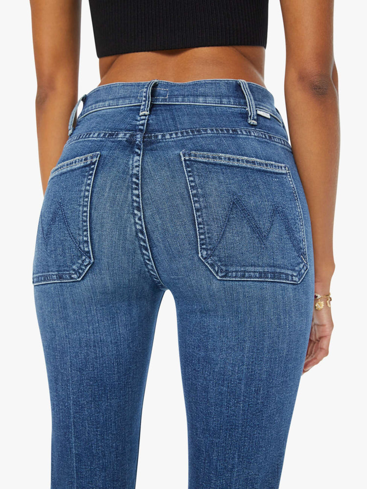 Close up view of a woman high-rise bootcut is designed with front patch pockets, a long 32-inch inseam and a clean hem in a mid blue wash.