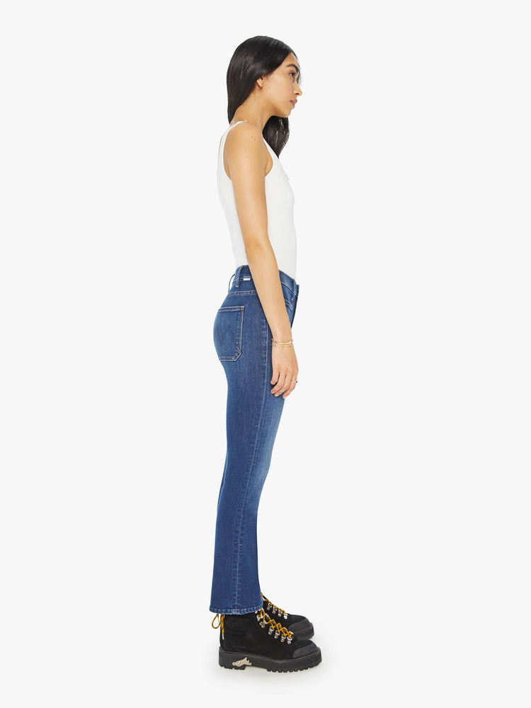 Side view of a woman in medium blue high-rise bootcut pants with front patch pockets and a clean hem. 