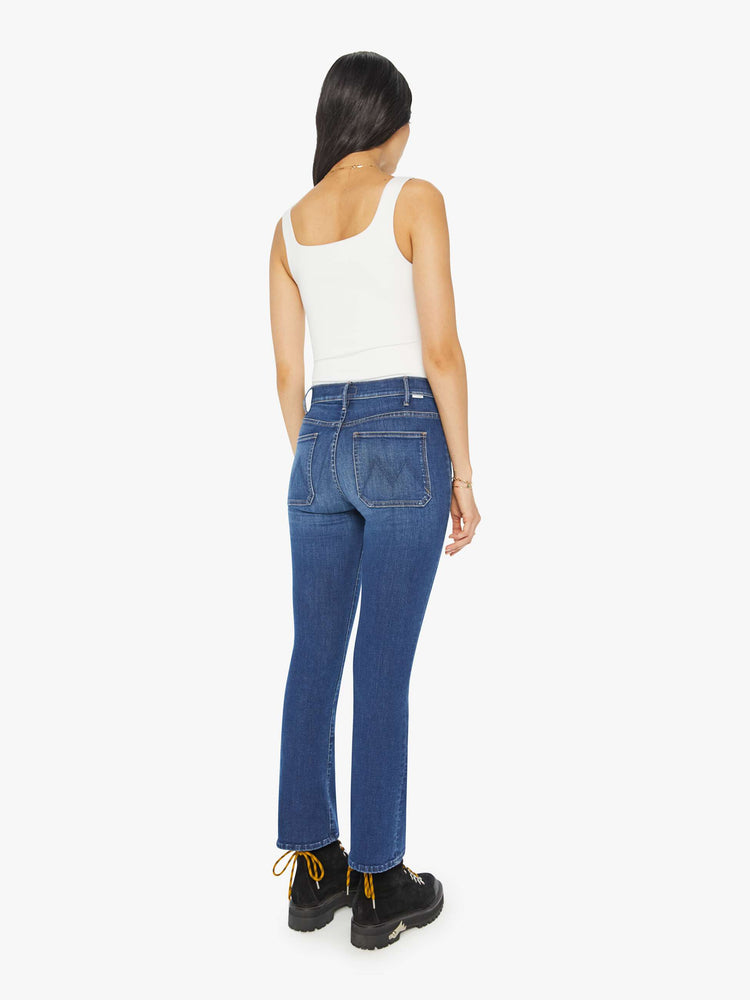 Back view of a woman in medium blue high-rise bootcut pants with front patch pockets and a clean hem. 