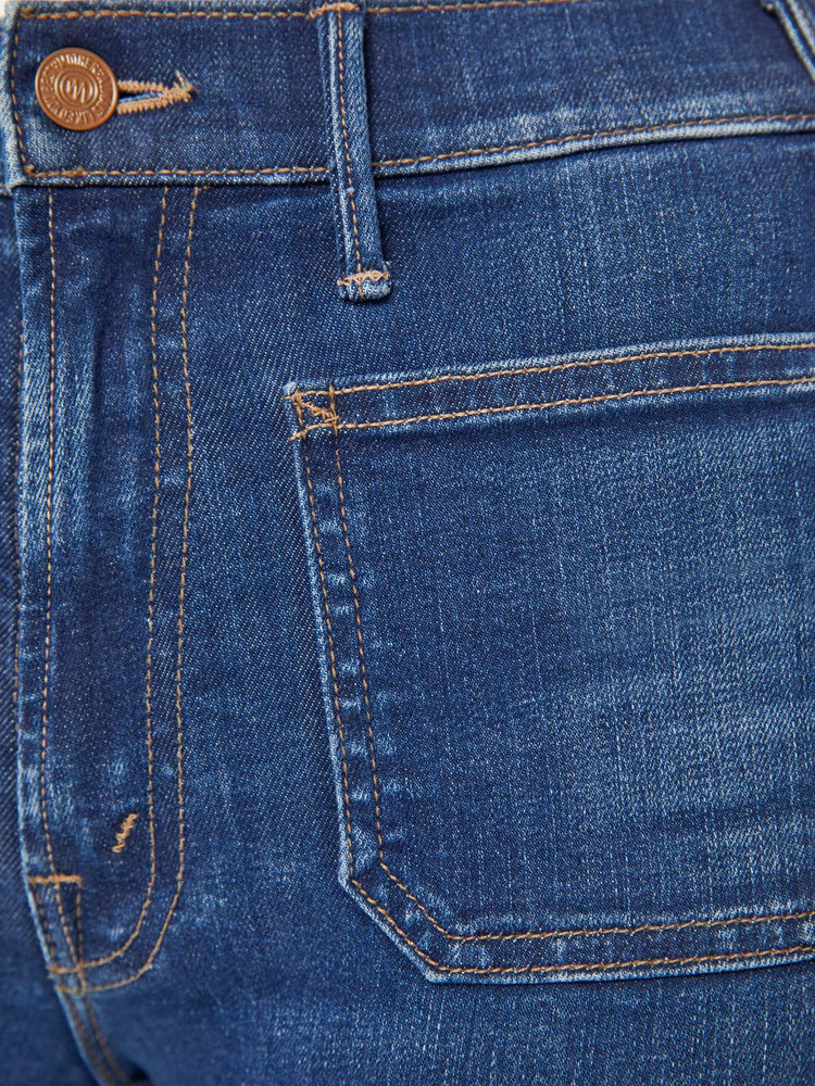 Detailed view of a woman in medium blue high-rise bootcut pants with front patch pockets and a clean hem. 