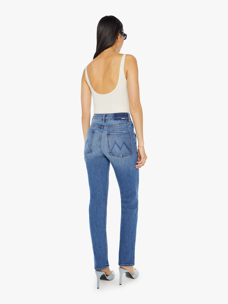 Back view of a woman in a mid blue high rise jean with a narrow straight leg, triangle pockets and a 31-inch inseam with a clean hem.