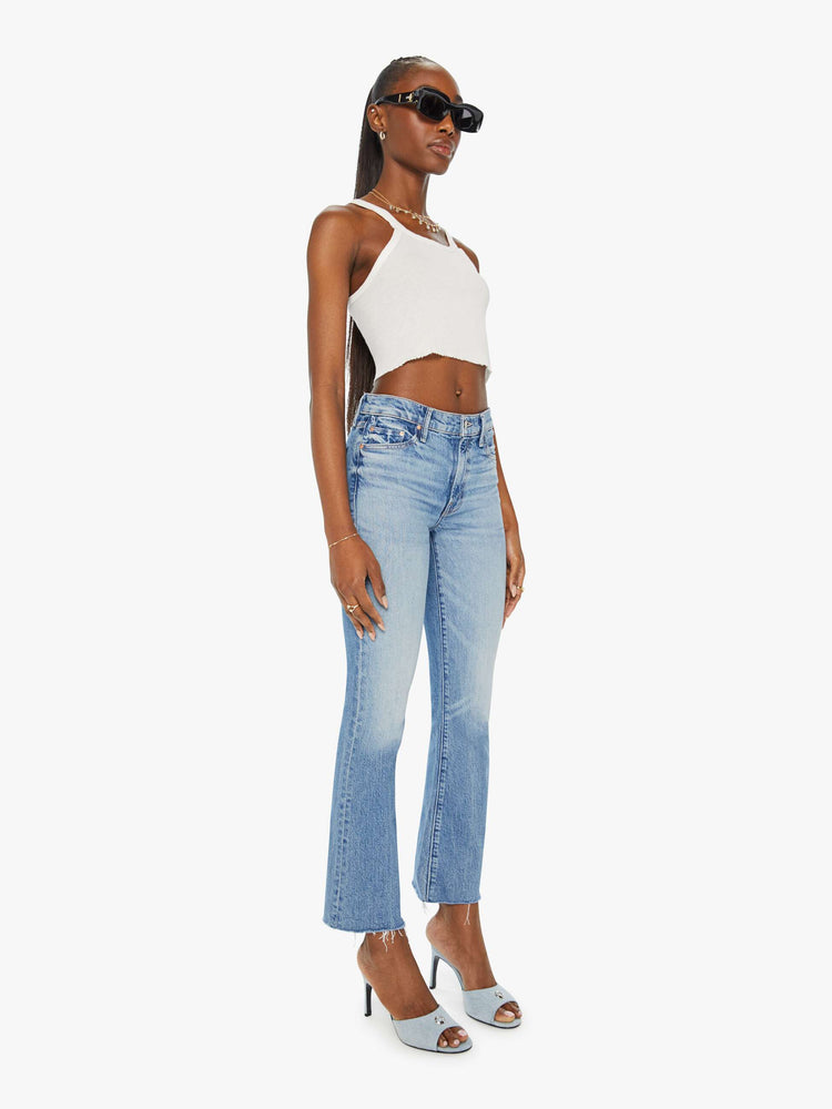 Angled front view of a woman in narrow flare light blue mid rise jeans with a frayed hem.