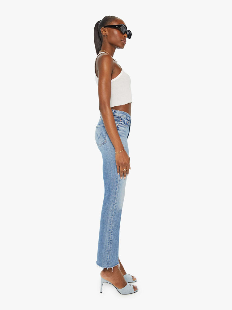 Side view of a woman in narrow flare light blue mid rise jeans with a frayed hem.