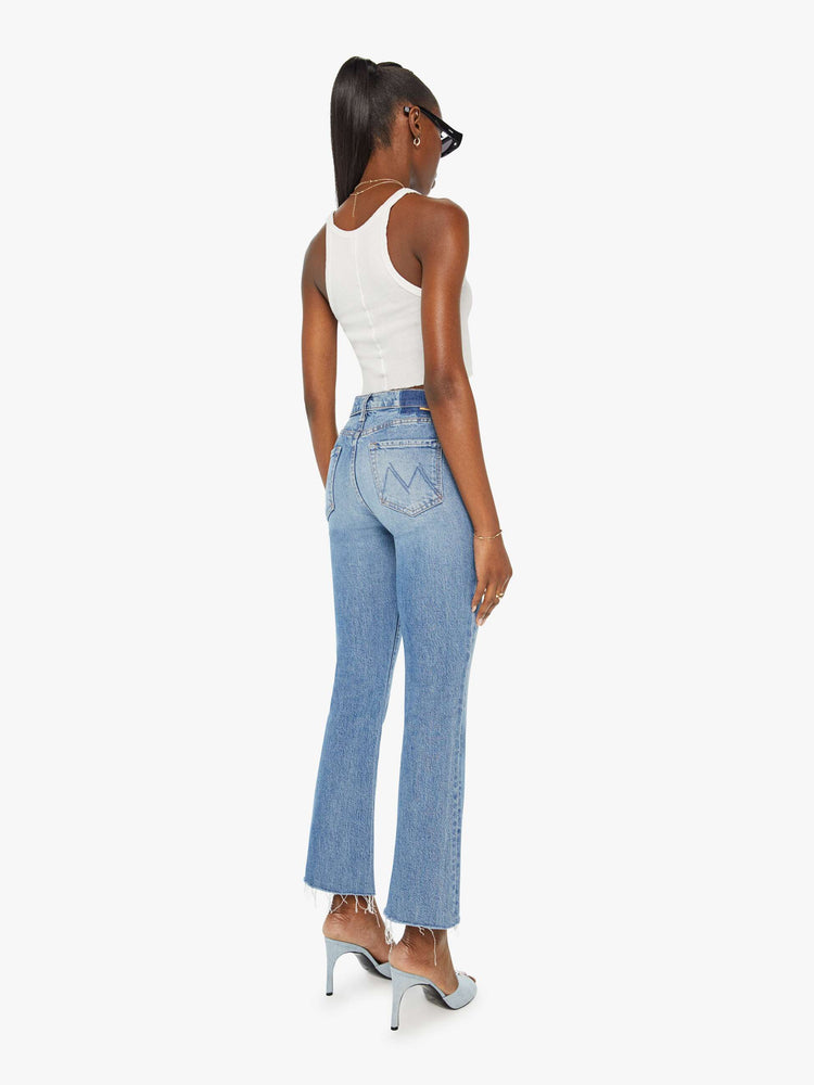 Back view of a woman in narrow flare light blue mid rise jeans with a frayed hem.