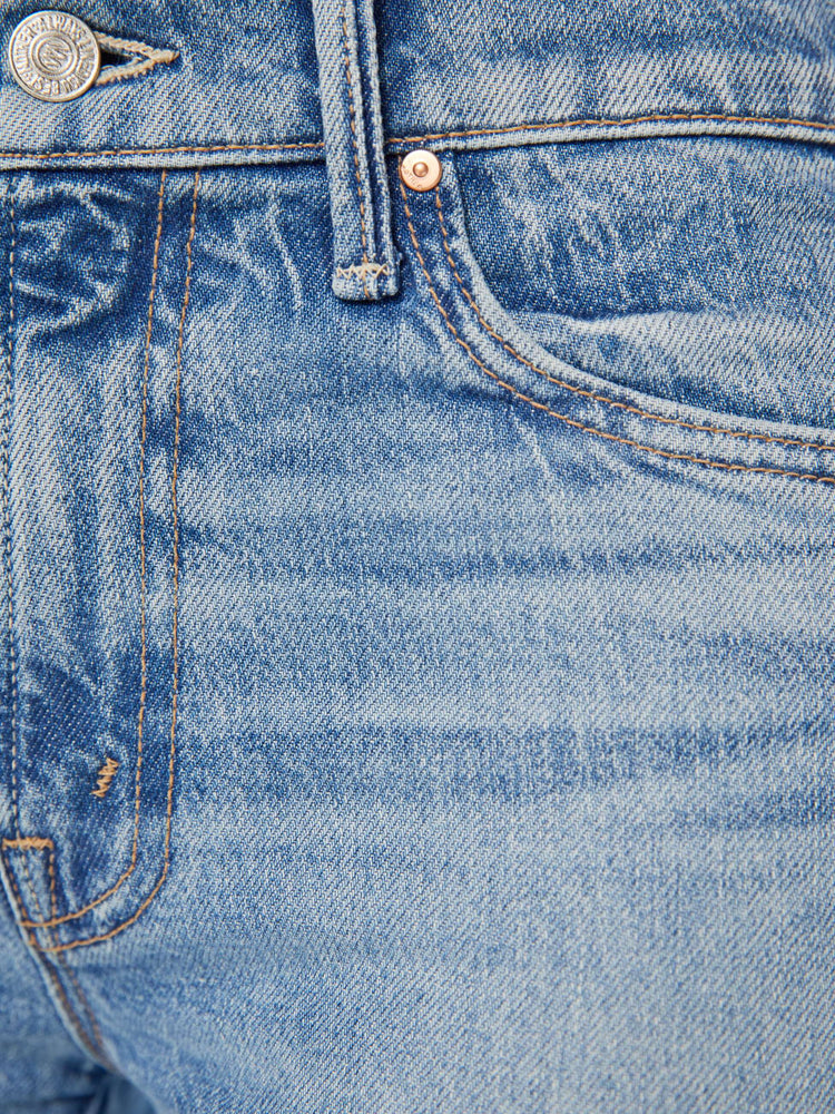 Detailed view of a woman in narrow flare light blue mid rise jeans with a frayed hem.