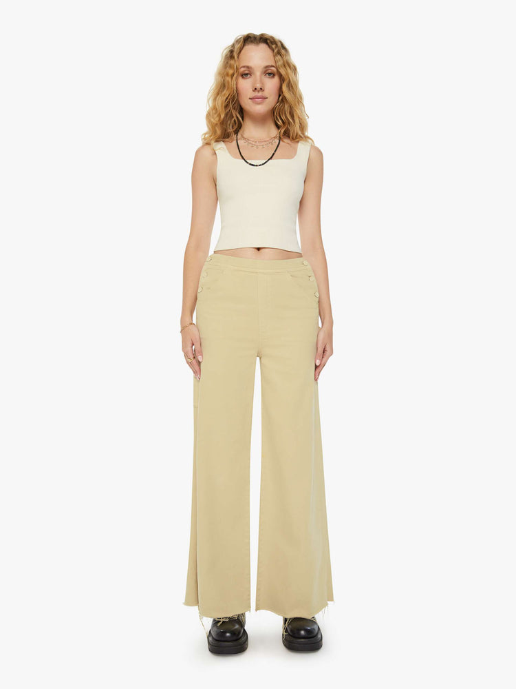 Front view of a woman in super high waisted light khaki wide-leg pants with buttoned details at the hips, utility-inspired patch pockets, a hammer loop and a long 32-inch inseam with a frayed hem. 