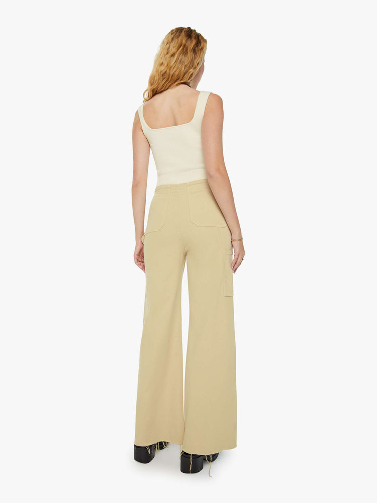 Back view of a woman in super high waisted light khaki wide-leg pants with buttoned details at the hips, utility-inspired patch pockets, a hammer loop and a long 32-inch inseam with a frayed hem. 