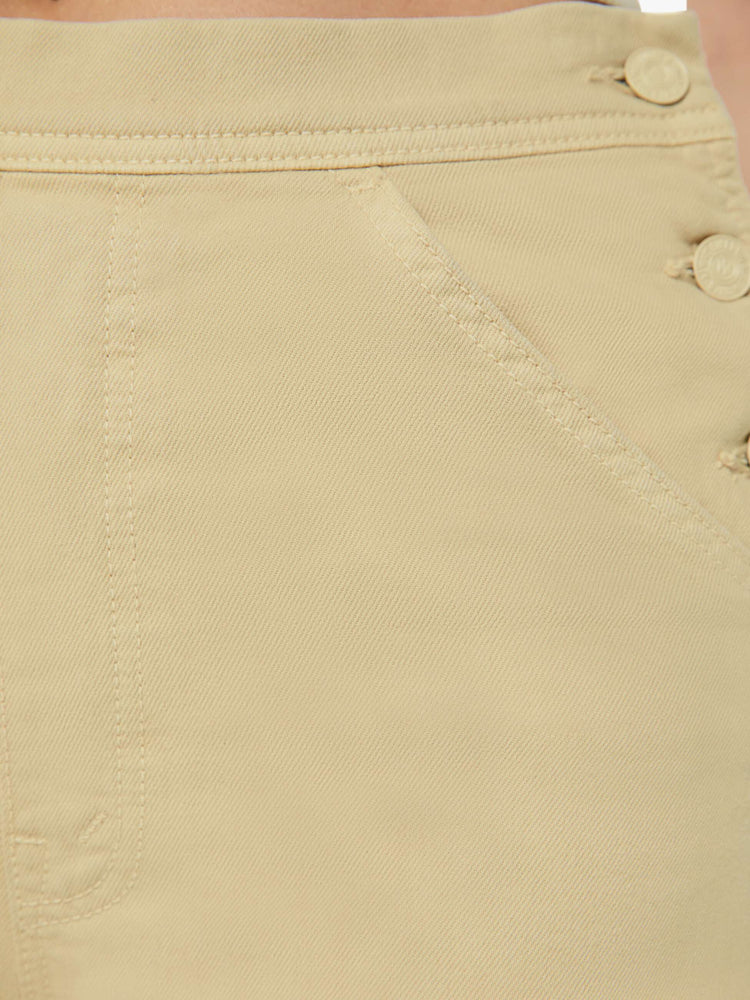 Detailed view of a woman in super high waisted light khaki wide-leg pants with buttoned details at the hips, utility-inspired patch pockets, a hammer loop and a long 32-inch inseam with a frayed hem. 