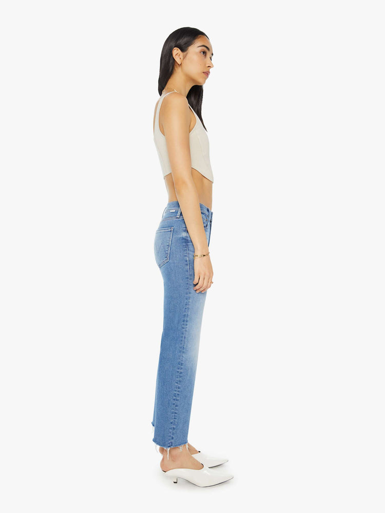 Side view of a woman in light blue mid-rise jeans with a wide straight leg, zip fly, an ankle-length inseam and a frayed hem.