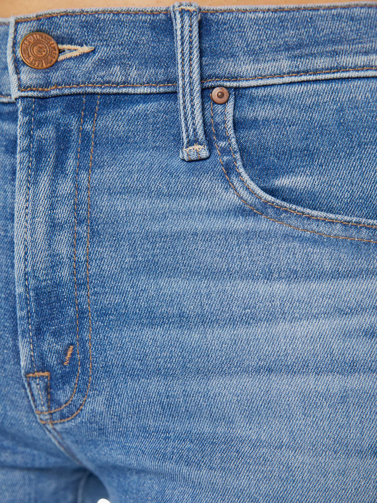 Detailed view of a woman in light blue mid-rise jeans with a wide straight leg, zip fly, an ankle-length inseam and a frayed hem.