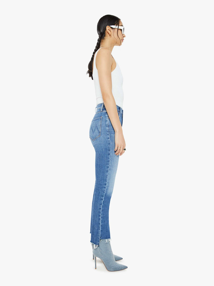 Side view of a mid blue high-rise straight-leg jeans with an ankle-length inseam and a frayed step-hem.