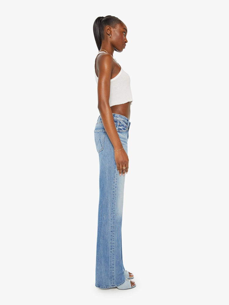 Side view of a woman in light blue mid-rise bootcut designed for a looser fit through the leg while fitted throughout the waist and hips. 