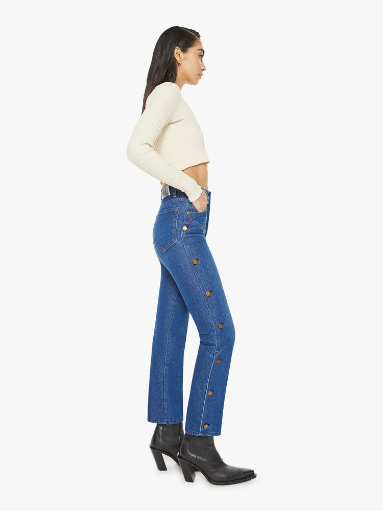 Side view of a woman in a high rise straight leg jean with chaps inspired buttons down each side with a 29 inch inseam in a classic blue.