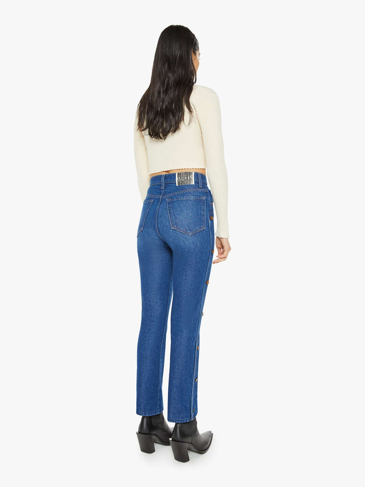 Back view of a woman in a high rise straight leg jean with chaps inspired buttons down each side with a 29 inch inseam in a classic blue.