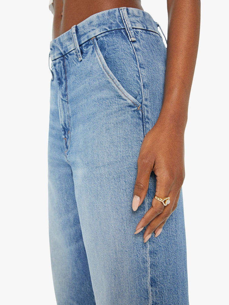 Detailed view of a woman in light blue high rise jeans that sit lower with slit pockets and a clean hem. 