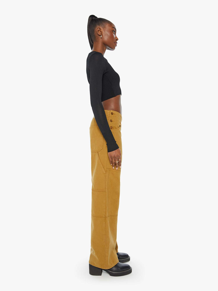 Side view of a woman in golden khaki wide-leg pants designed with a high rise, buttons at the hips, workwear-inspired patches at the knees, utility pockets, and a hammer loop.