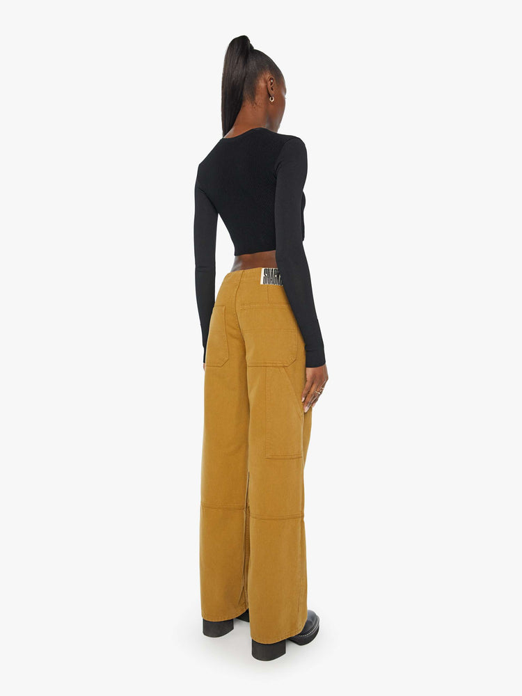 Back view of a woman in golden khaki wide-leg pants designed with a high rise, buttons at the hips, workwear-inspired patches at the knees, utility pockets, and a hammer loop.